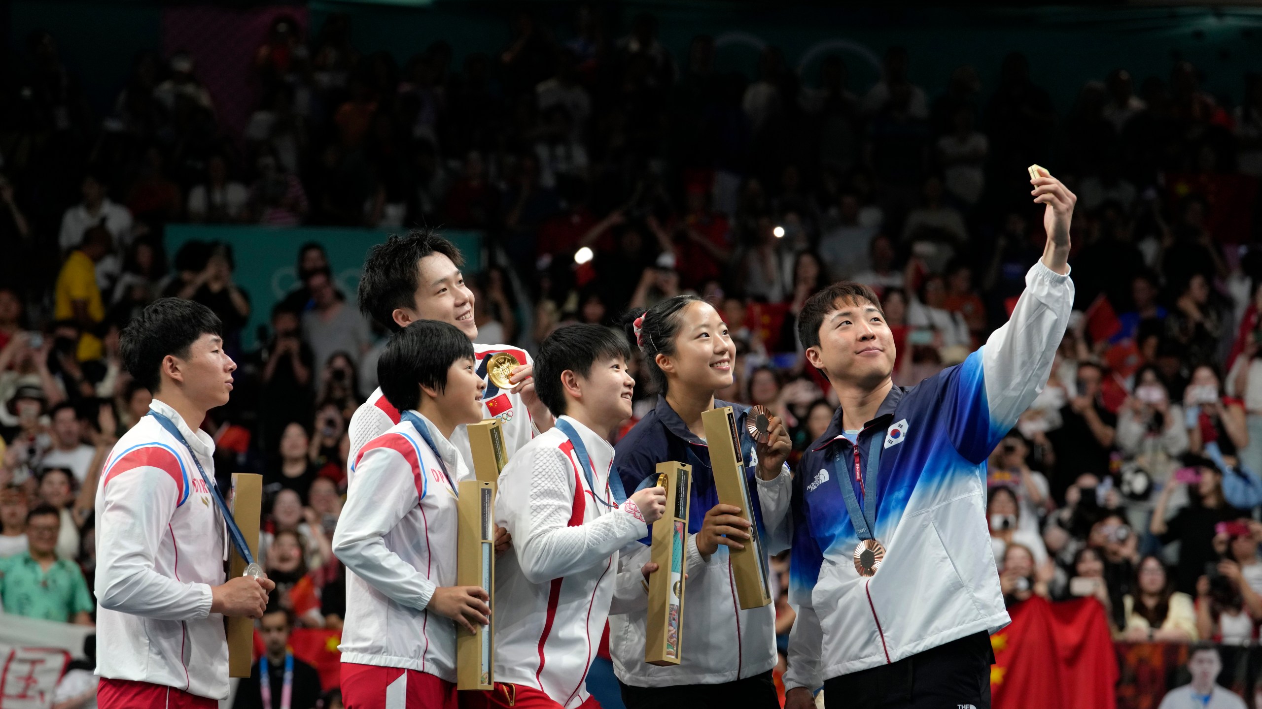 FILE - South Korea's Lim Jonghoon, right, takes a selfie with North Korea's Ri Jong Sik, left, and Kim Kum, second left, China's Wang Chuqin, background, and Sun Yingsha, center, and his teammate Shin Yubin, right, and Lim Jonghoon during the medal ceremony at the 2024 Summer Olympics, July 30, 2024, in Paris, France. (AP Photo/Petros Giannakouris, File)