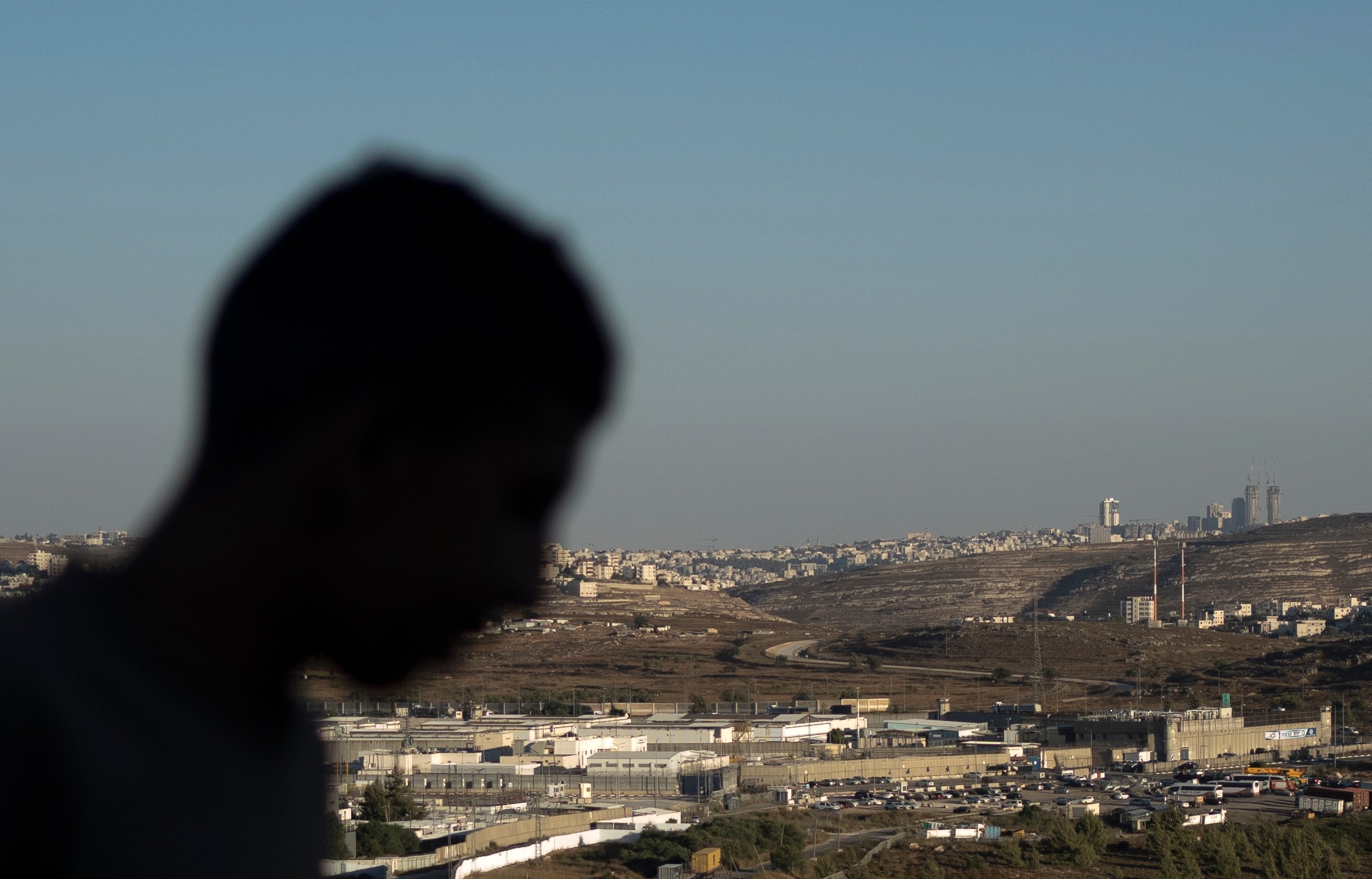 A Palestinian youth stands on a hill overlooking Israel's Ofer Prison, near the West Bank city of Ramallah, Wednesday, July 3, 2024. Five released Palestinians told The Associated Press of dramatically worsening treatment in prisons crowded with new detainees from the West Bank and Gaza over the past 10 months of war. (AP Photo/Maya Alleruzzo)