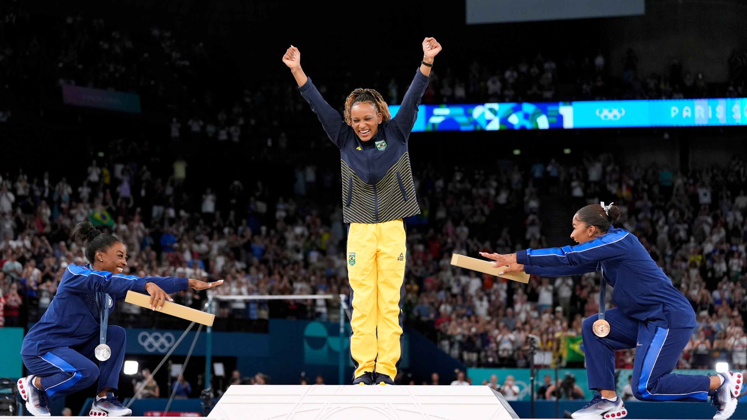 Silver medalist Simone Biles, of the United States, left, and bronze medalist Jordan Chiles, of the United States, right, bow to gold medalist Rebeca Andrade, of Brazil, during the medal ceremony for the women's artistic gymnastics individual floor finals at Bercy Arena at the 2024 Summer Olympics, Monday, Aug. 5, 2024, in Paris, France. (AP Photo/Abbie Parr)