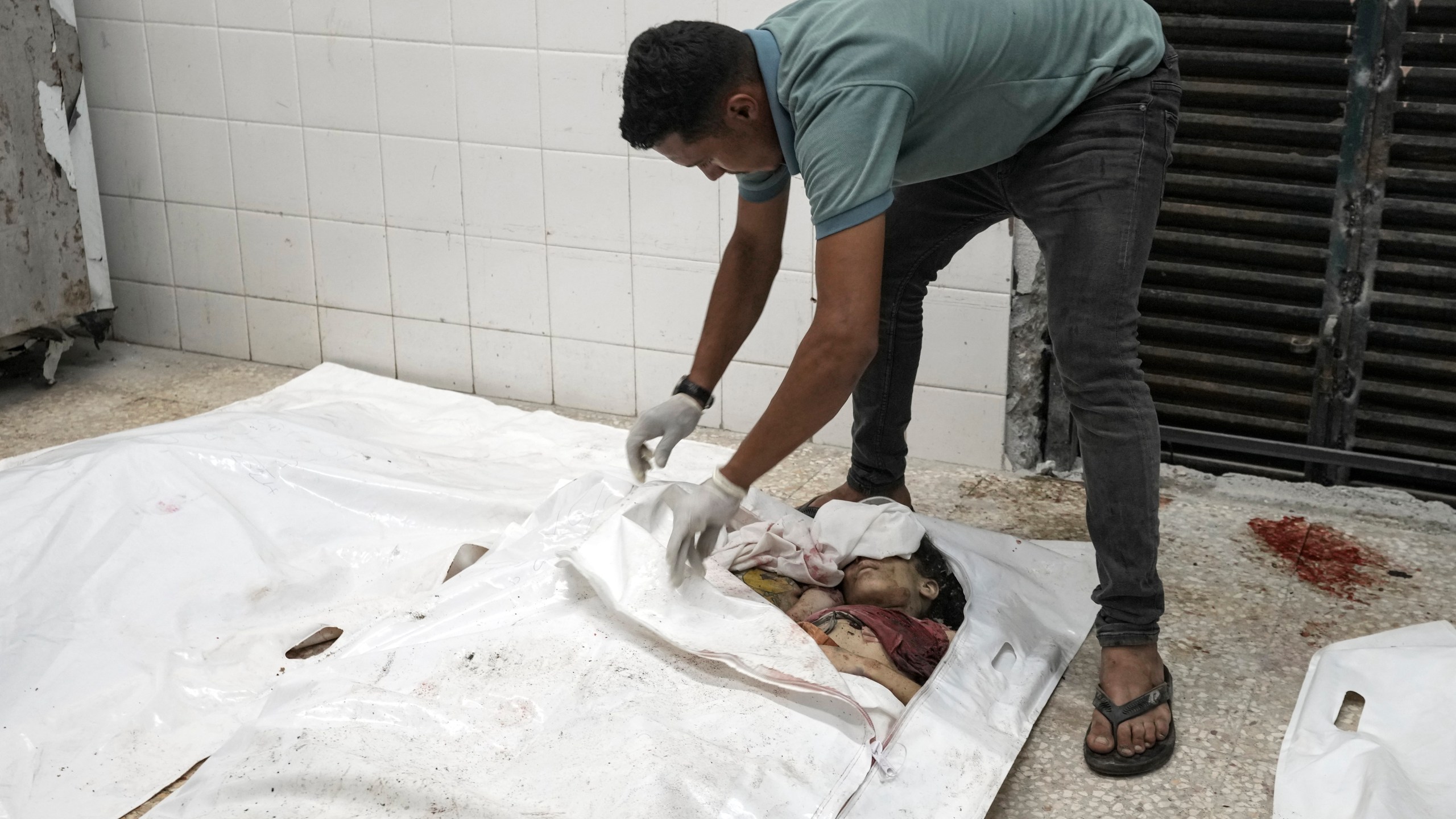 EDS NOTE: GRAPHIC CONTENT - A worker unzips a body bag to display a Palestinian family, consisting of five children aged 2 to 11 and their parents, in the morgue at Al-Aqsa Martyrs Hospital in Deir al-Balah, Gaza Strip, after an Israeli strike hit their home in the Nuseirat refugee camp, Wednesday, Aug. 14, 2024. (AP Photo/Abdel Kareem Hana)