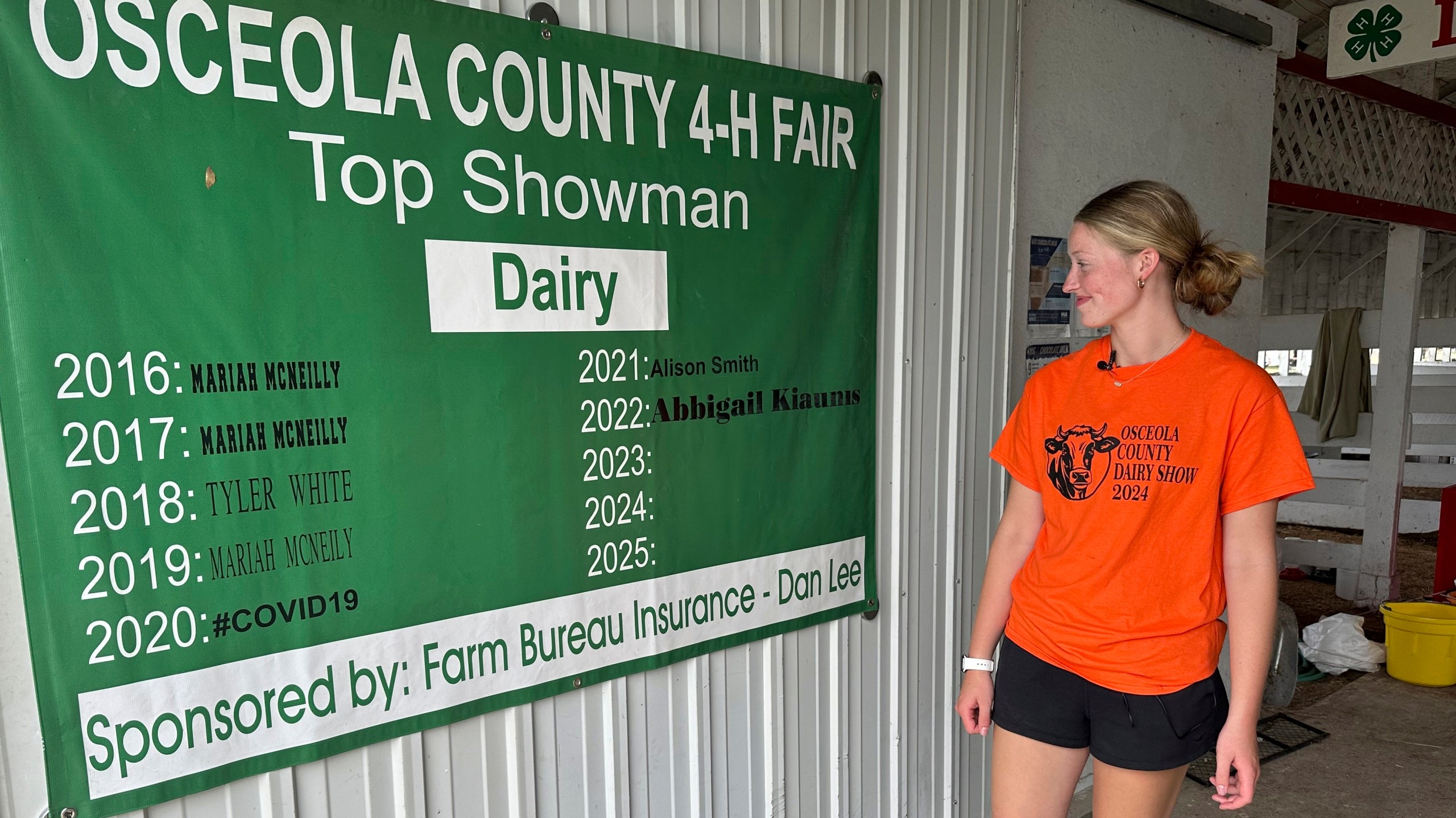 Osceola County 4-H member Alison Smith stands inside the dairy barn Thursday, Aug. 1, 2024, at the county fairgrounds in Evart, Mich. The banner shows that Smith was the 2021 recipient of the fair's dairy showman award (AP Photo/Mike Householder)