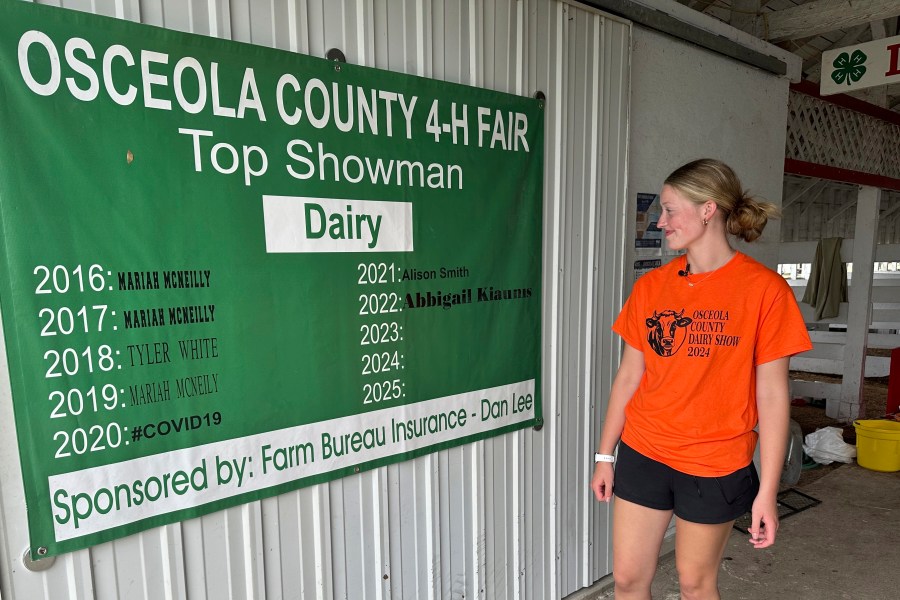 Osceola County 4-H member Alison Smith stands inside the dairy barn Thursday, Aug. 1, 2024, at the county fairgrounds in Evart, Mich. The banner shows that Smith was the 2021 recipient of the fair's dairy showman award (AP Photo/Mike Householder)