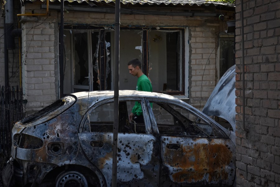 A man passes by a damaged car after a Russian rocket attack in Malokaterynivka, Zaporizhzhia region, Ukraine, Wednesday, Aug. 21, 2024. (AP Photo/Andriy Andriyenko)