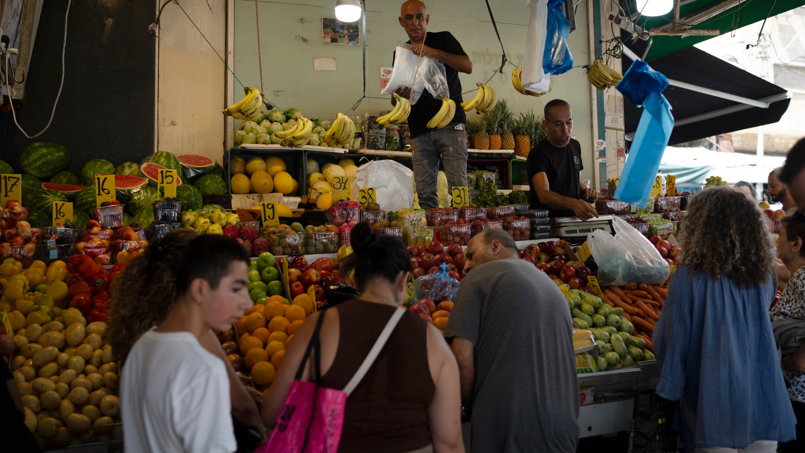 People buy fruit from a street market in Haifa, Israel, Friday, Aug. 16, 2024. Israel's economy is suffering from the nearly 11-month war with Hamas, as its leaders grind ahead with its offensive in Gaza that threatens to escalate into a wider conflict. (AP Photo/Leo Correa)