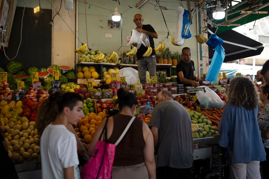 People buy fruit from a street market in Haifa, Israel, Friday, Aug. 16, 2024. Israel's economy is suffering from the nearly 11-month war with Hamas, as its leaders grind ahead with its offensive in Gaza that threatens to escalate into a wider conflict. (AP Photo/Leo Correa)