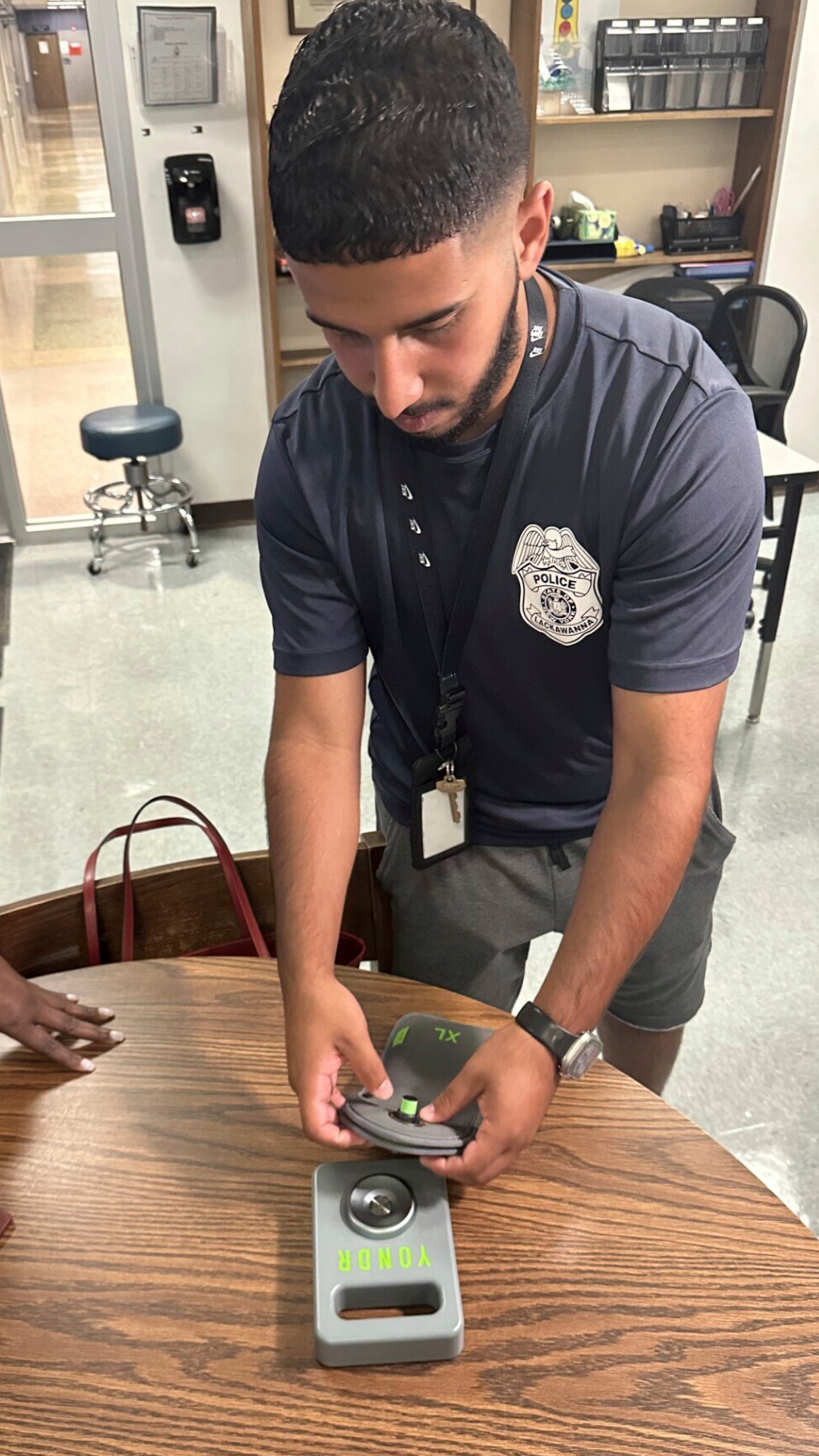 Lackawanna Police Officer Abdul Albaneh, who works with schools, demonstrates how to unlock a cellphone pouch that will prevent students from using their cellphones during the school day to improve student engagement, in Lackawanna, N.Y., Aug. 19, 2024, for when school resumes in September. (AP Photo/Carolyn Thompson)