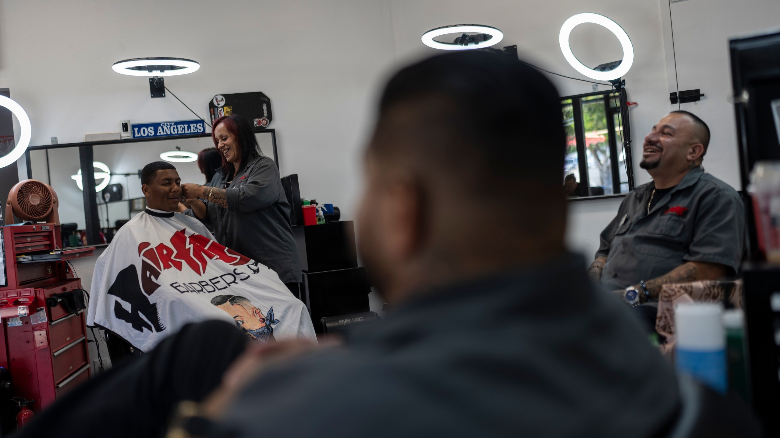 Adelita Valentine, second from left, owner of HairFreek Barbers, shares a light moment with other barbers while giving a haircut to Cameron Loualhati in Los Angeles, Wednesday, Aug. 21, 2024. (AP Photo/Jae C. Hong)