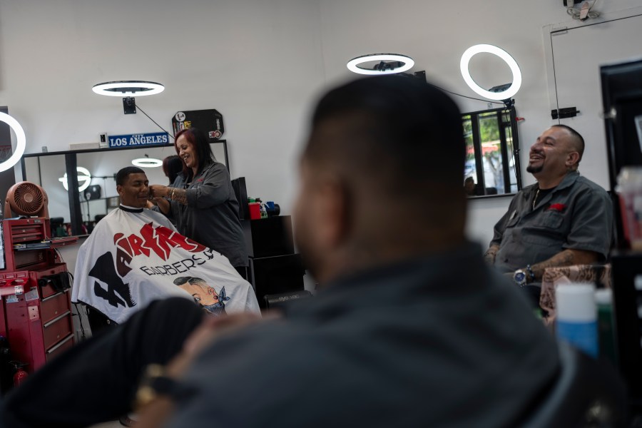 Adelita Valentine, second from left, owner of HairFreek Barbers, shares a light moment with other barbers while giving a haircut to Cameron Loualhati in Los Angeles, Wednesday, Aug. 21, 2024. (AP Photo/Jae C. Hong)