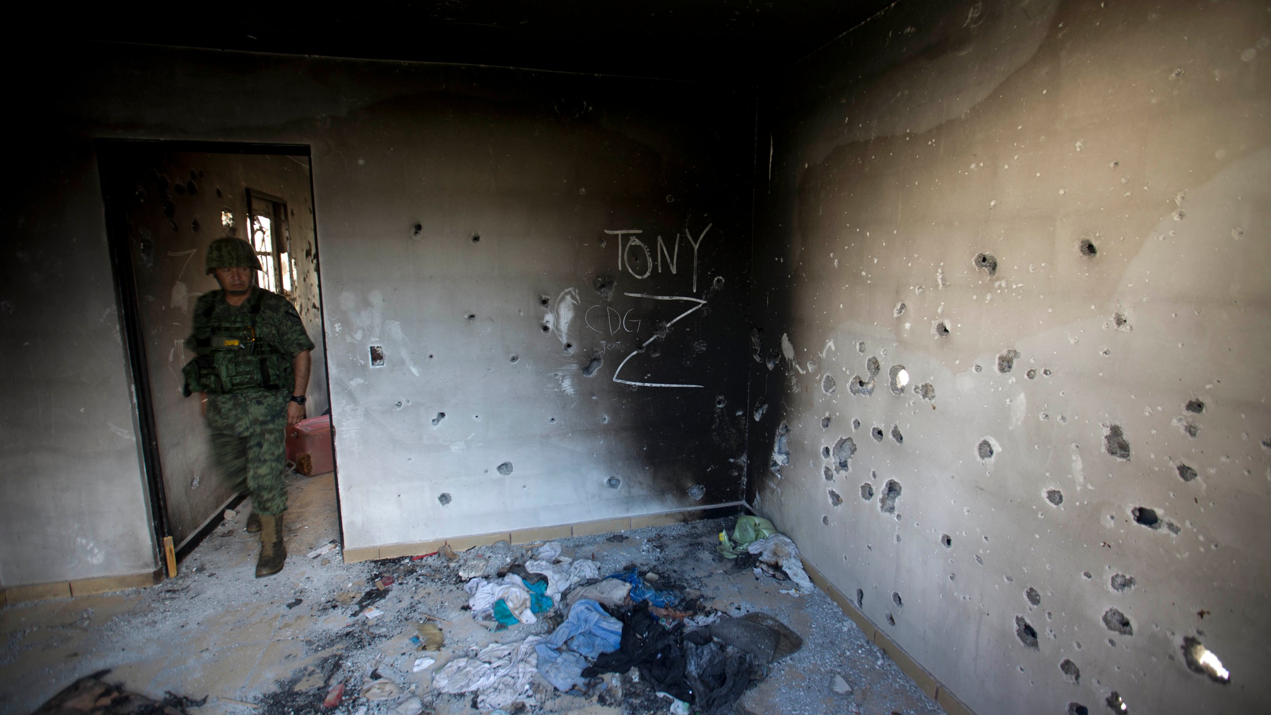 FILE - A soldier enters a bullet-riddled home covered by the initials of the Gulf Cartel (CDG) and Zetas (Z) in Ciudad Victoria, Tamaulipas state, Mexico, Sept. 6, 2014. (AP Photo/Eduardo Verdugo, File)