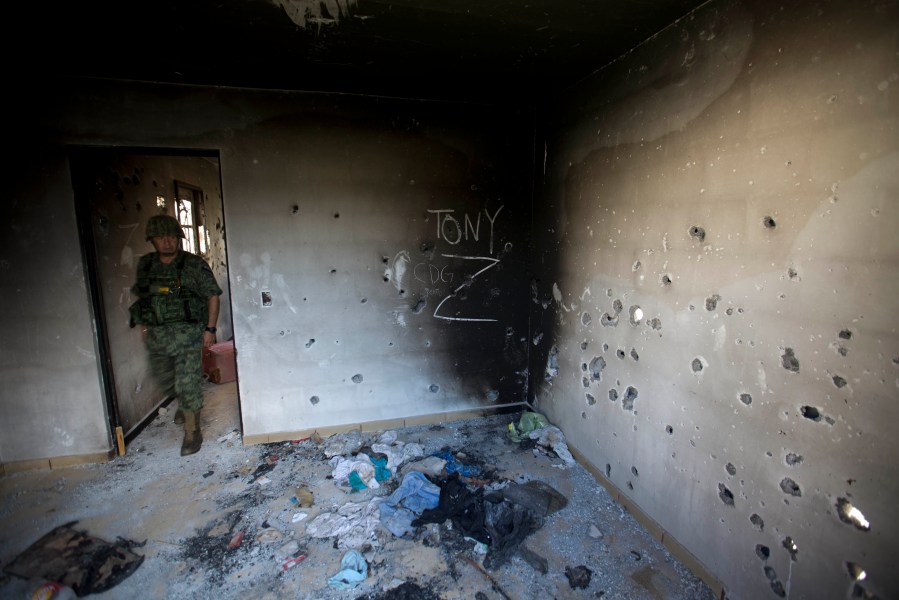 FILE - A soldier enters a bullet-riddled home covered by the initials of the Gulf Cartel (CDG) and Zetas (Z) in Ciudad Victoria, Tamaulipas state, Mexico, Sept. 6, 2014. (AP Photo/Eduardo Verdugo, File)