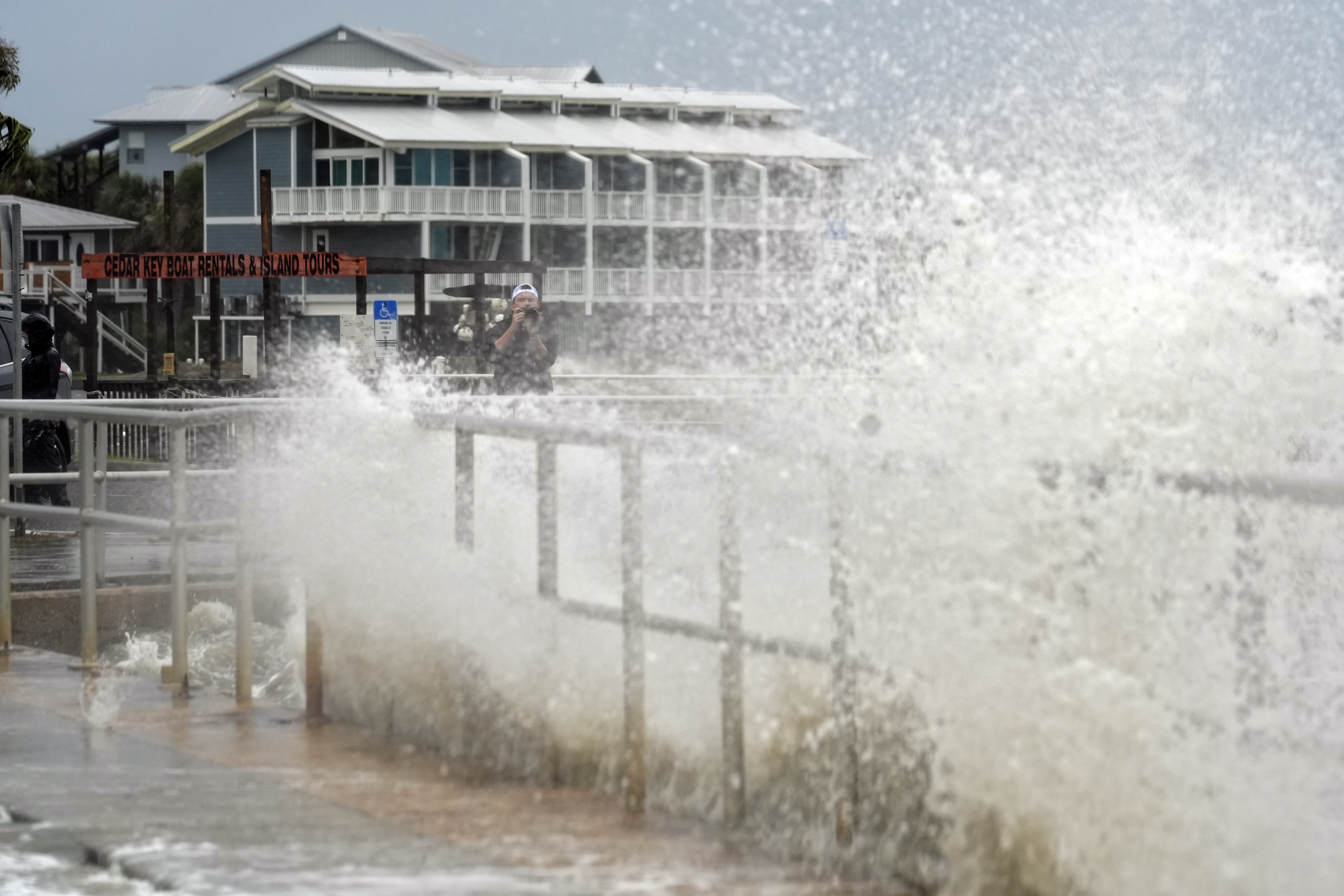 A man takes photos of the surf pushed by winds from Tropical Storm Debby as they break over the sea wall in Cedar Key, Fla., on Sunday, Aug. 4, 2024.