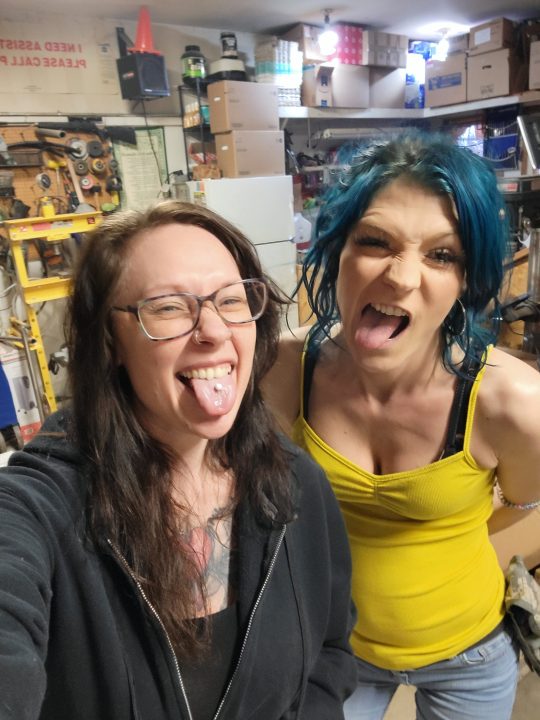 Two women sticking their tongues out, one with teal hair.