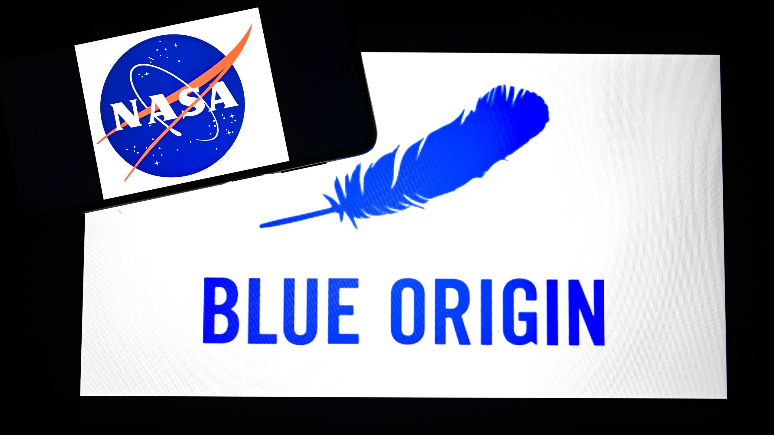 The logo of NASA is displayed on mobile phone screen in front of Blue Origin icon