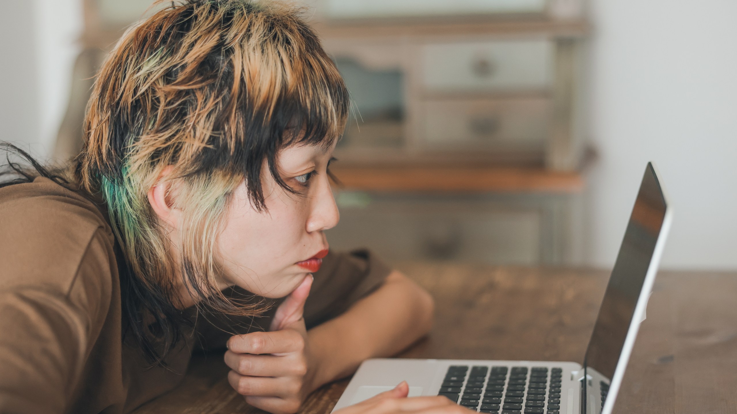 Close up shot of young Asian Gen-Z female with colorful hair at a cafe or Home struggling to find work while searching on her laptop.