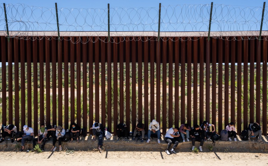 Migrants sit by an iron fence waiting to be processed by the U.S. Border Patrol.