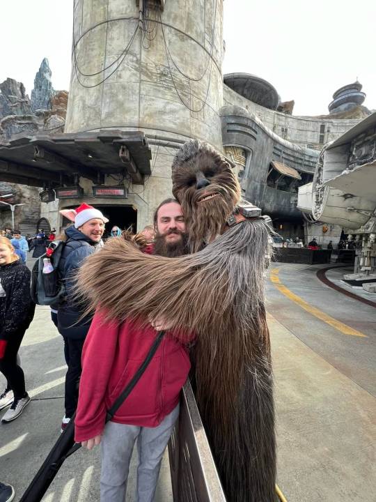 A young bearded man being hugged by Chewbacca.