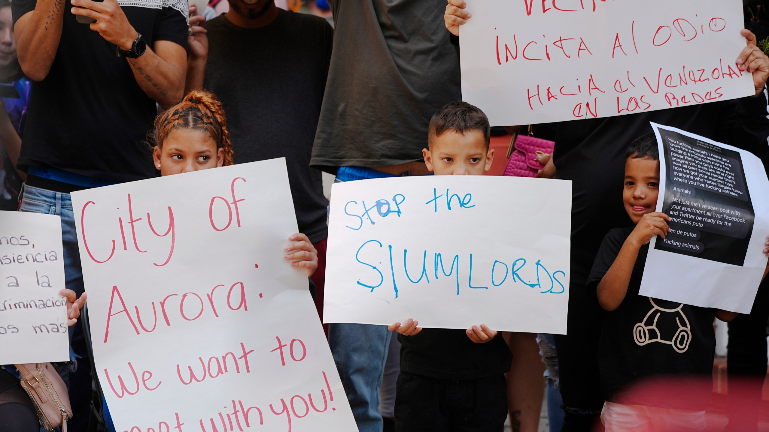 Residents hold up placards during a rally staged by the East Colfax Community Collective to address chronic problems in the apartment buildings occupied by people displaced from their home countries in central and South America Tuesday, Sept. 3, 2024, in Aurora, Colo. (AP Photo/David Zalubowski)