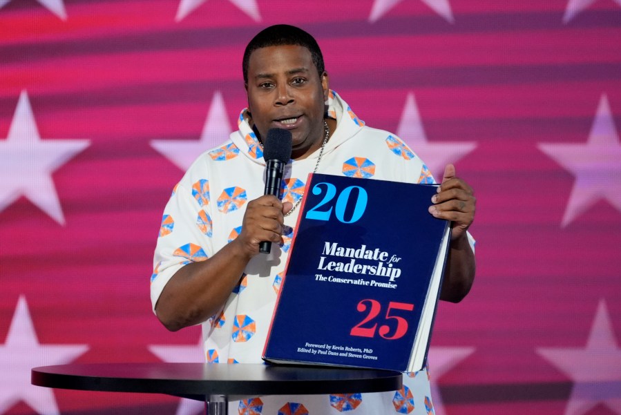 Kenan Thompson speaks as he carries a copy of Project 2025 on stage during the Democratic National Convention Wednesday, Aug. 21, 2024, in Chicago. (AP Photo/J. Scott Applewhite)