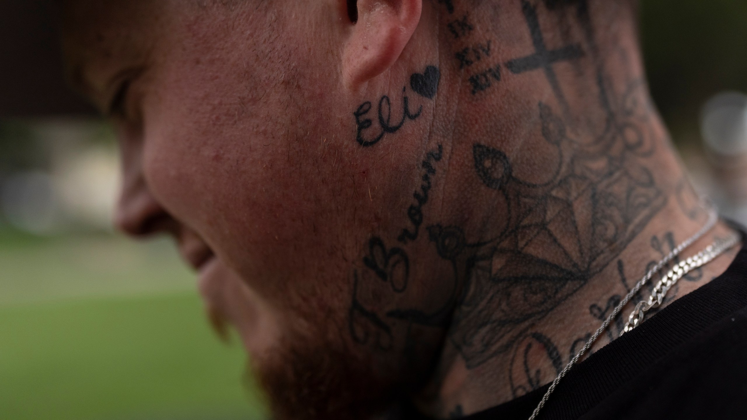 With his stepson's name tattooed below his ear, Tyler Brown, stepfather of Elijah Ott, who died of a fentanyl overdose at 15, looks at a park bench dedicated to Elijah in Paso Robles, Calif., Friday, Aug. 2, 2024. (AP Photo/Jae C. Hong)