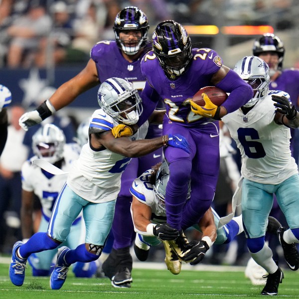 Baltimore Ravens running back Derrick Henry (22) runs the ball as Dallas Cowboys' Jourdan Lewis (2), Eric Kendricks, bottom, and Donovan Wilson (6) attempt to make the stop in the first half of an NFL football game in Arlington, Texas, Sunday, Sept. 22, 2024. (AP Photo/Julio Cortez)