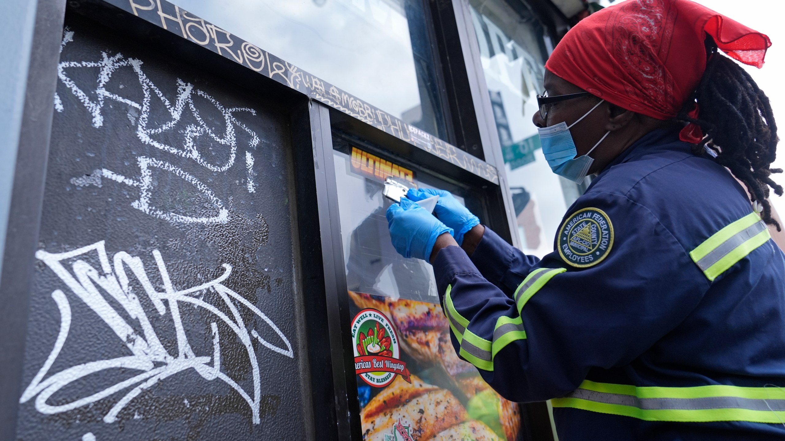 Queen Jones removes a sticker and graffiti in a neighborhood of Washington, Tuesday, Aug. 20, 2024. (AP Photo/Susan Walsh)