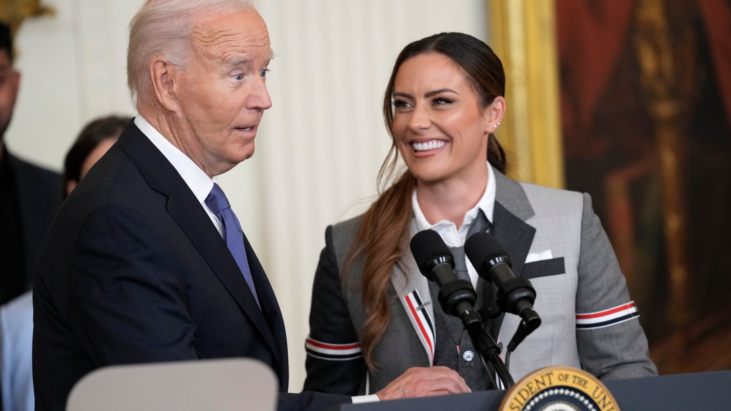 President Joe Biden speaks as Ali Krieger, right, a member of the 2023 NWSL championship NJ/NY Gotham FC team, listens during an event in the East Room of the White House in Washington, Monday, Sept. 23, 2024, to welcome the team and celebrate their championship. (AP Photo/Susan Walsh)