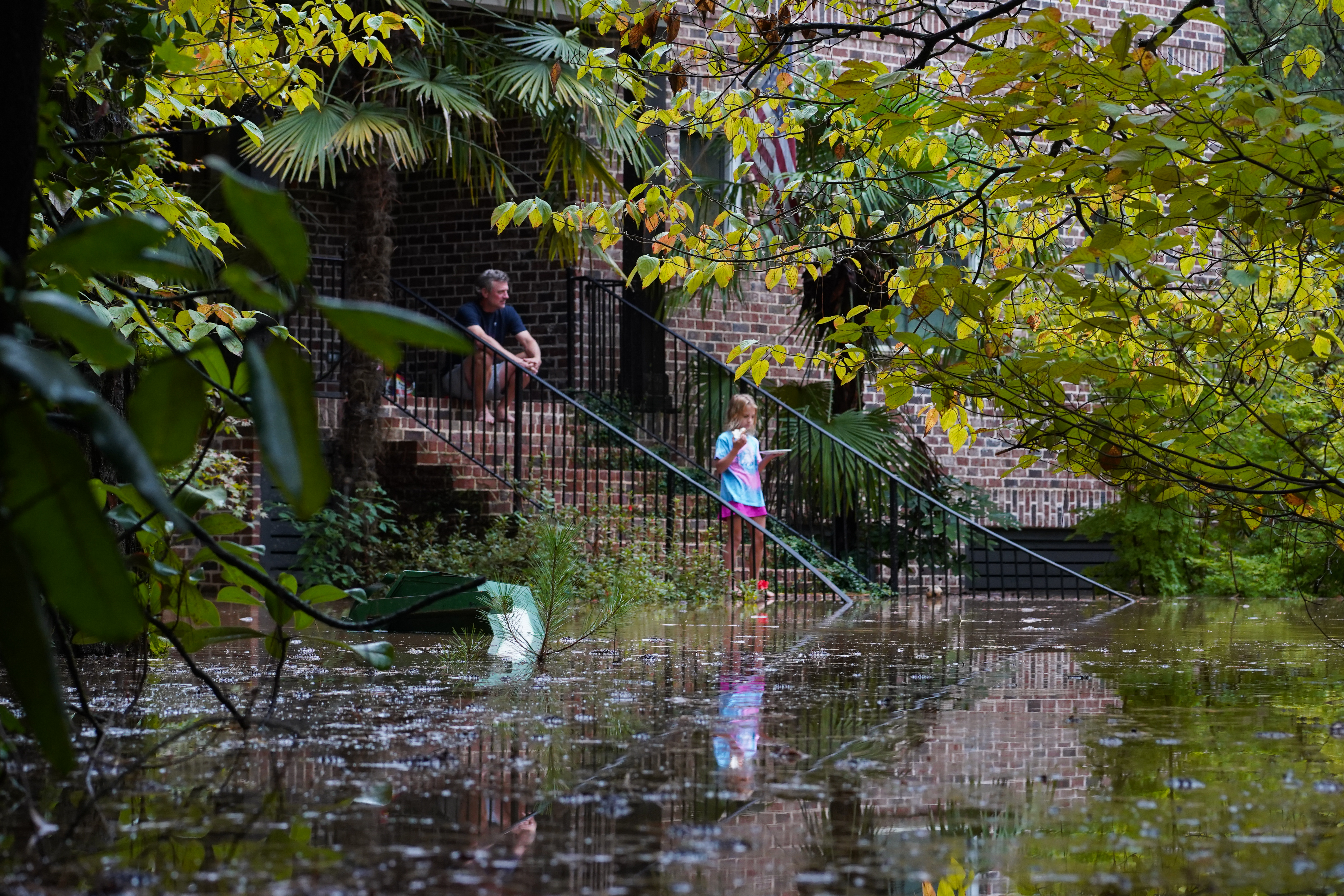 Brandon Walton and his daughter sit on their steps after just moving back into their home last night following a fire on New Year as the streets are flooded near Peachtree Creek after hurricane Helene brought in heavy rains overnight on September 27, 2024 in Atlanta, Georgia.