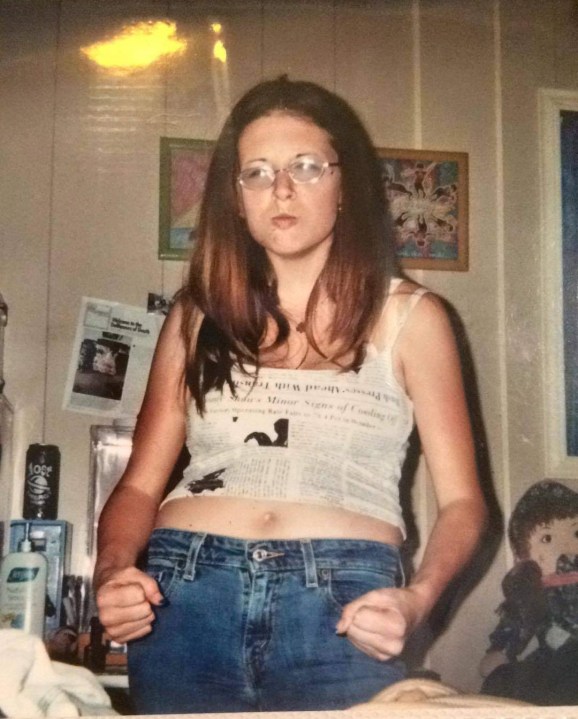 A girl in a tank top and jeans with glasses, posing in a silly way.