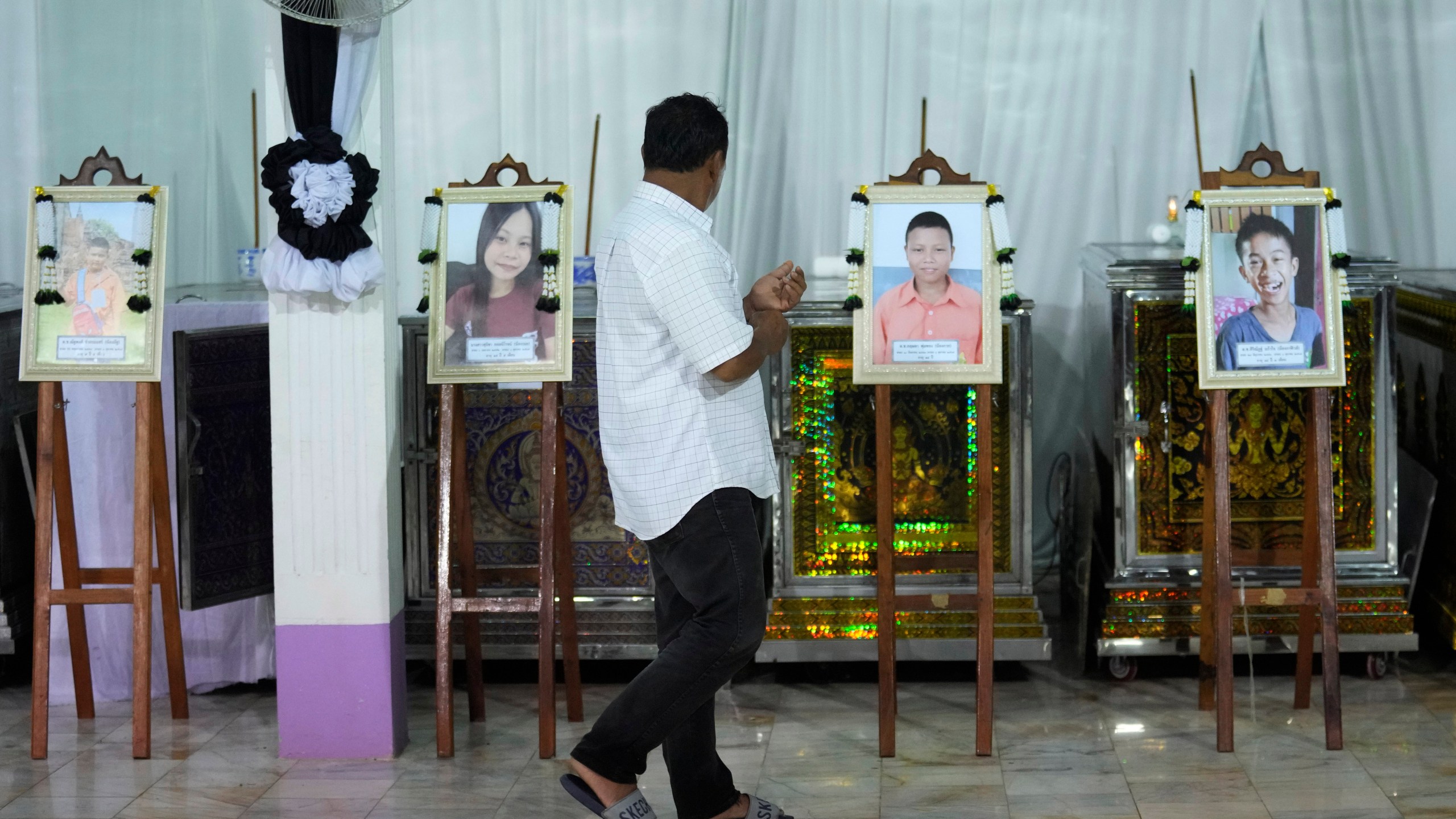 A relative of the bus fire victims walks in front of their coffins at the Wat Khao Phraya Sangkharam School Lan Sak , Uthai Thani province, Thailand, Wednesday, Oct. 2, 2024. (AP Photo/Sakchai Lalit)