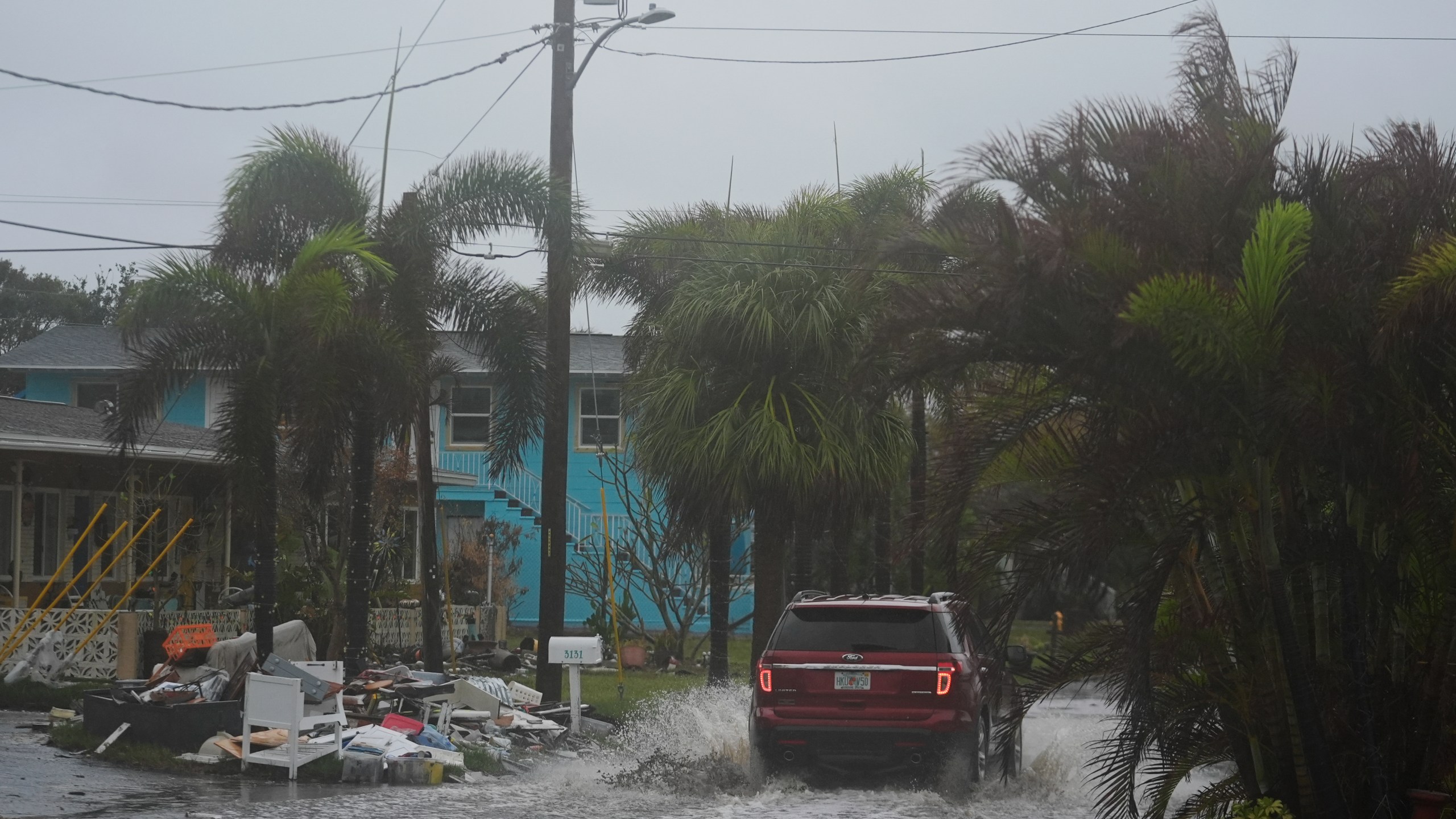 A car drives past a pile of debris from Hurricane Helene flooding, along a street that had already begun flooding from rain ahead of the arrival of Hurricane Milton, in Gulfport, Fla., Wednesday, Oct. 9, 2024. (AP Photo/Rebecca Blackwell)