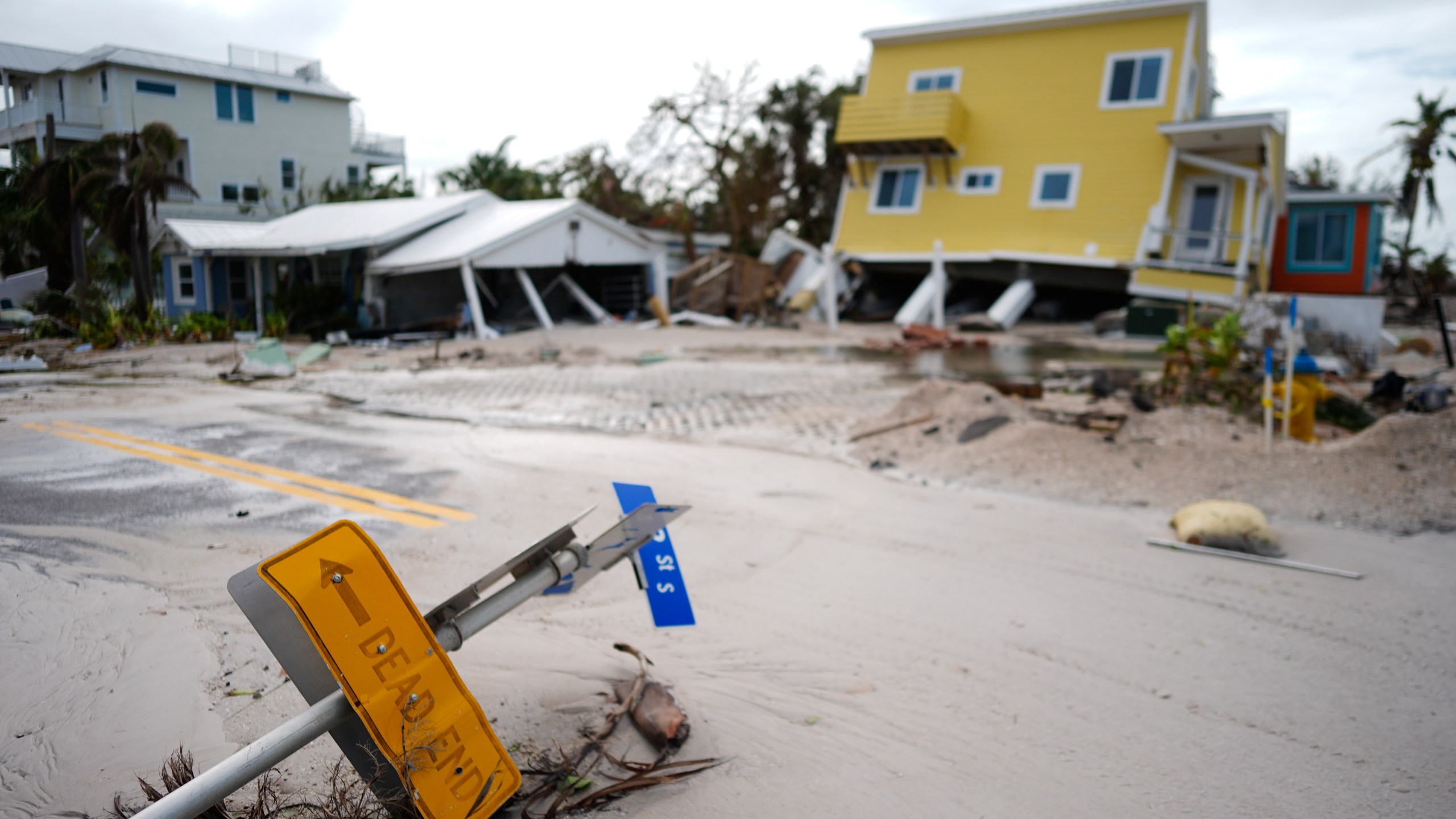 A house sits toppled off its stilts after the passage of Hurricane Milton, alongside an empty lot where a home was swept away by Hurricane Helene, in Bradenton Beach on Anna Maria Island, Fla., Thursday, Oct. 10, 2024. (AP Photo/Rebecca Blackwell)