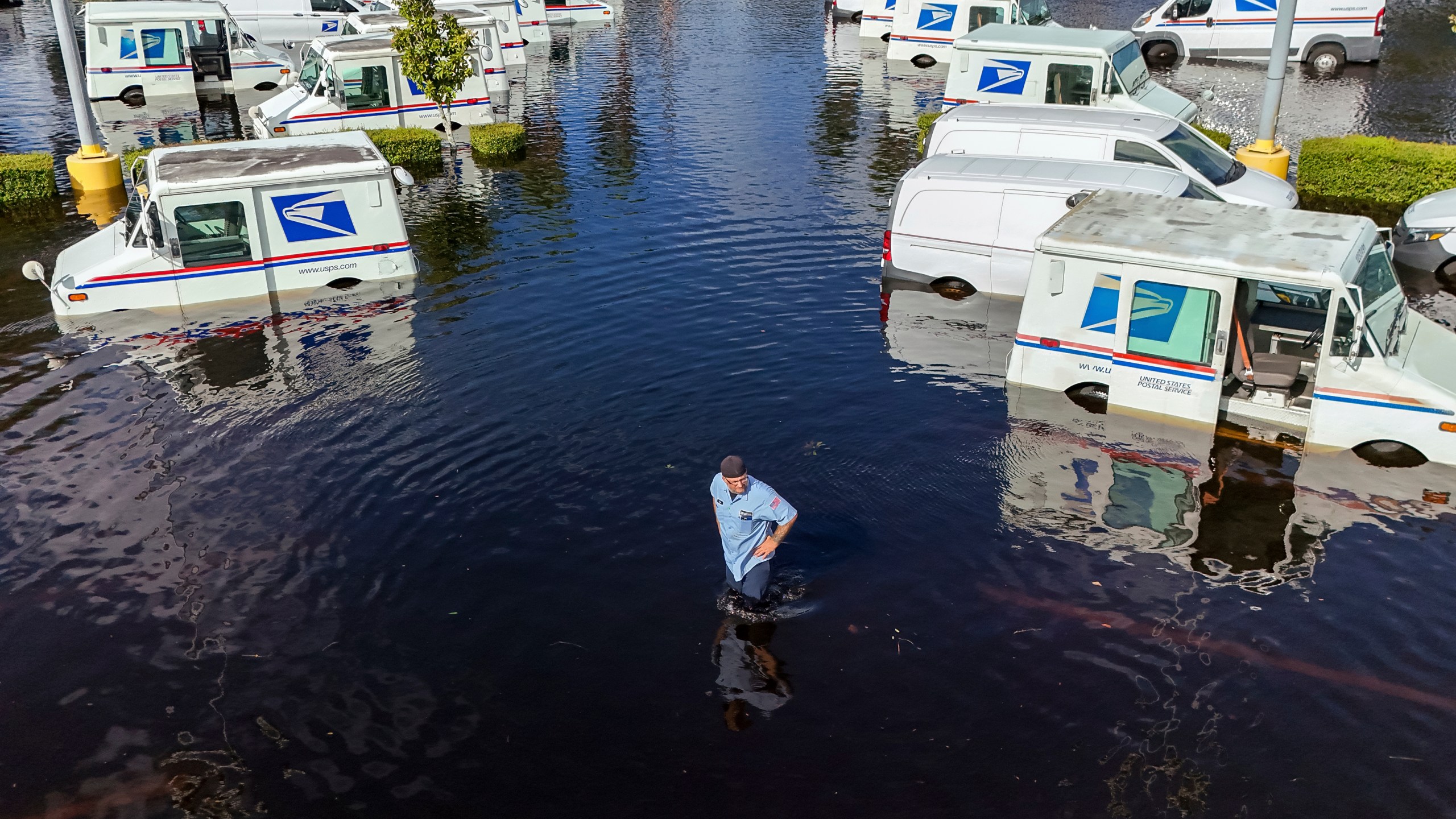 A USPS worker inspects trucks that had been relocated to protect them from wind but which are now underwater as intense rain from Hurricane Milton caused the Anclote River to flood, Friday, Oct. 11, 2024, in New Port Richey, Fla. (AP Photo/Mike Carlson)