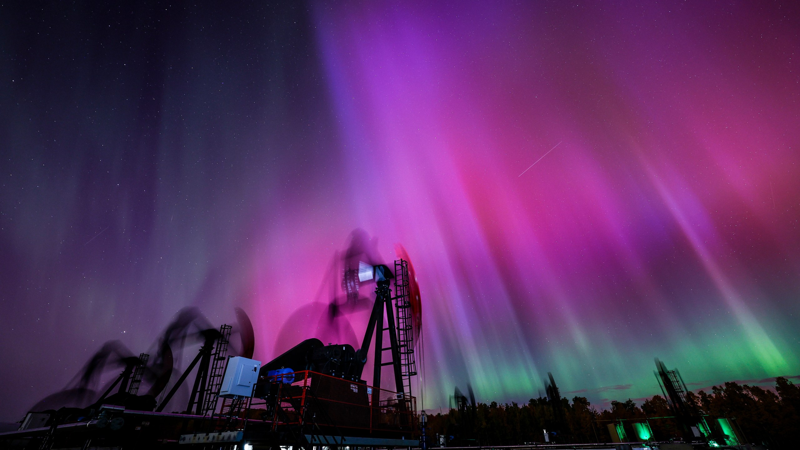 An aurora borealis, also known as the northern lights, makes an appearance over pumpjacks as they draw out oil and gas from well heads near Cremona, Alberta, Thursday, Oct. 10, 2024. (Jeff McIntosh/The Canadian Press via AP)