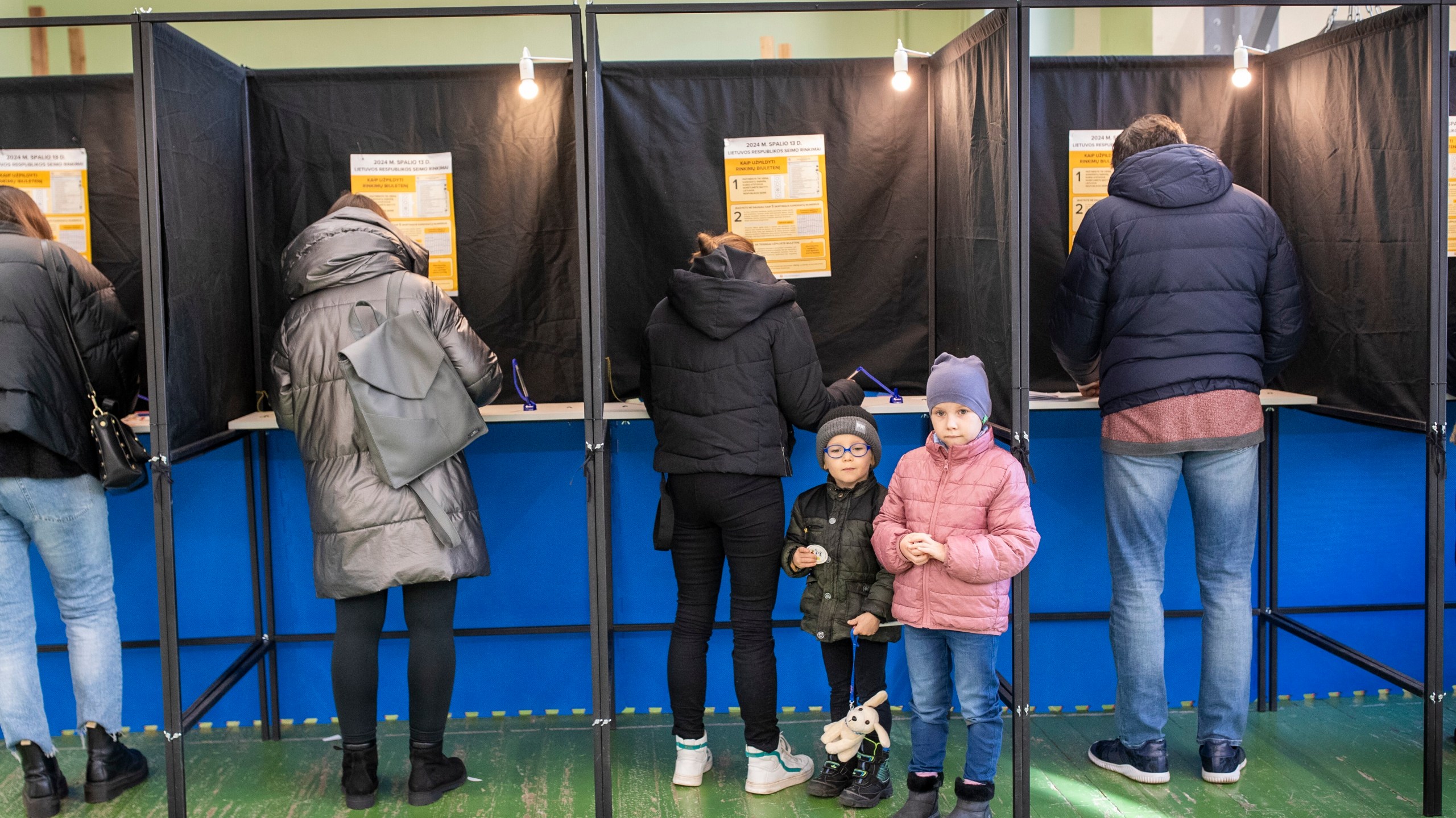 A children stand near a voting booth during the first round of voting in parliamentary election, in Vilnius, Lithuania, Sunday, Oct. 13, 2024. (AP Photo/Mindaugas Kulbis)