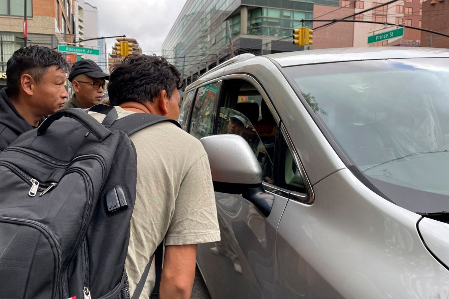 FILE - Wang Gang, 36, front, a Chinese immigrant, talks with the driver of a car with others as they try to get a daily paid job working construction or in another trade in the Flushing neighborhood of the Queens borough of New York on May 3, 2024. (AP Photo/Fu Ting, File)