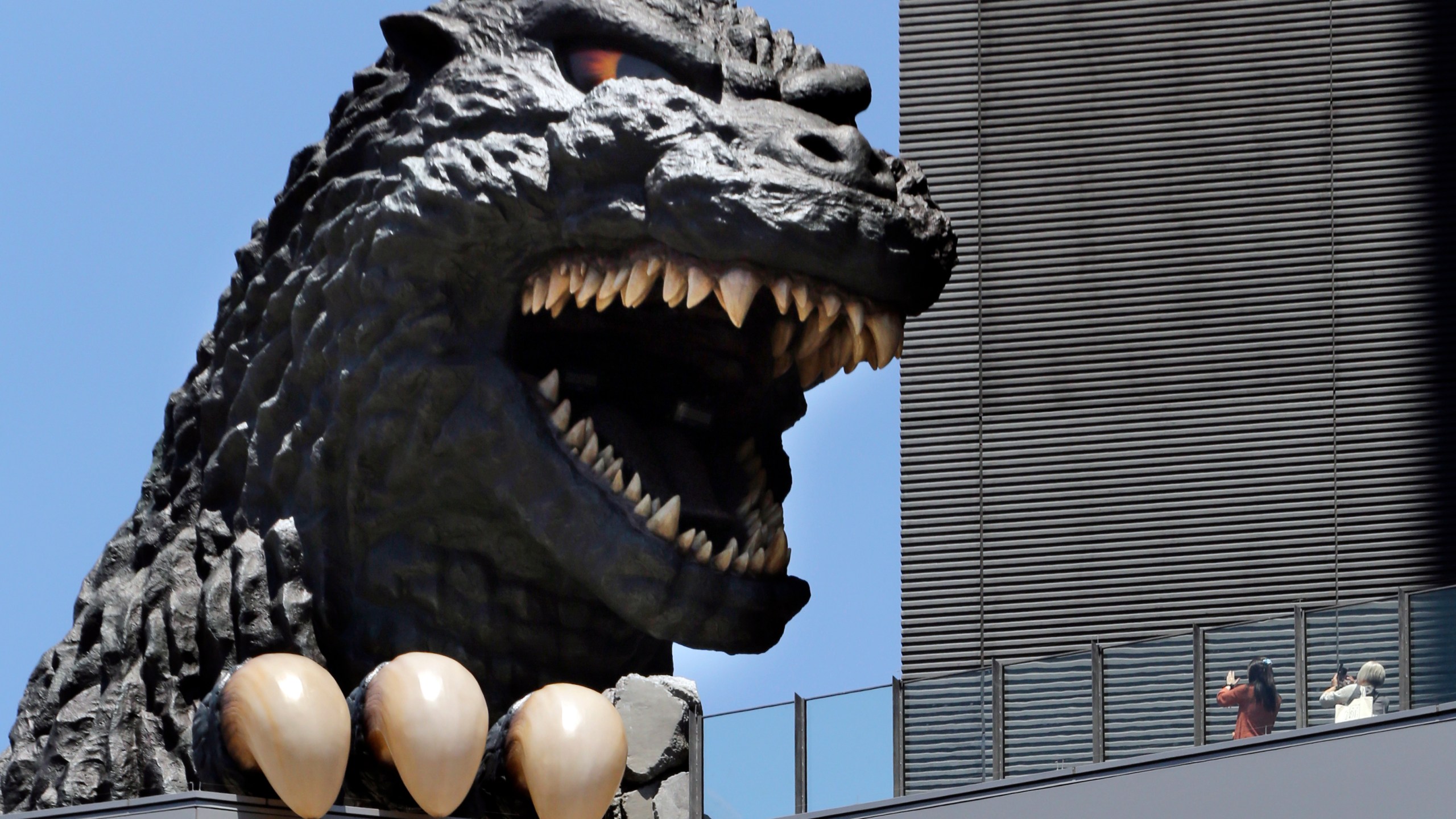 FILE - People take a picture of Godzilla's head at Shinjyuku Toho building at the Kabukicho district in Tokyo, July 30, 2016. (AP Photo/Koji Sasahara, File)