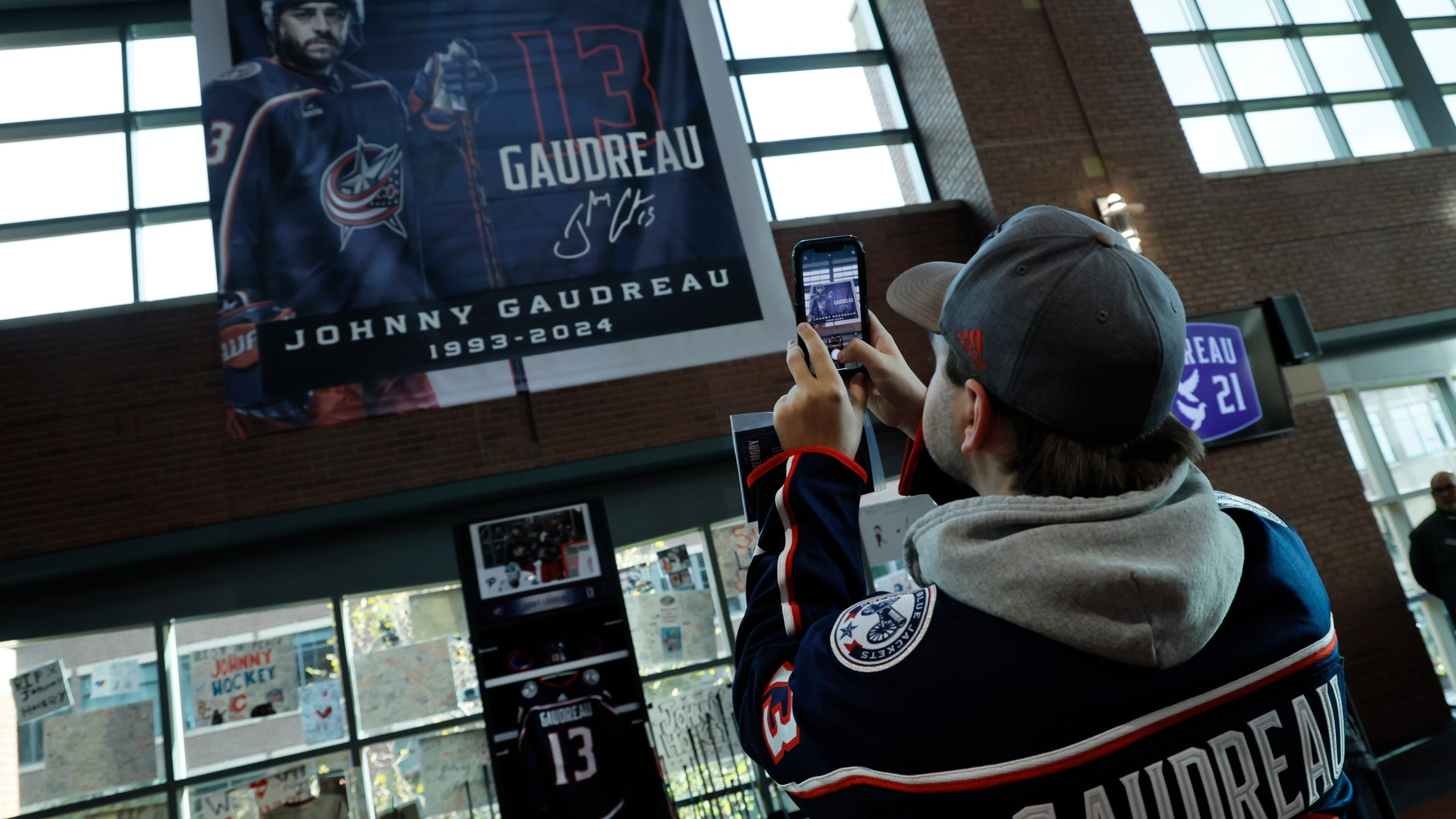 Troy Ward, of Dayton, takes photos of a memorial of Columbus Blue Jackets' Johnny Gaudreau and his brother Matthew before the start of an NHL hockey game against the Florida Panthers. Tuesday, Oct. 15, 2024, in Columbus, Ohio. (AP Photo/Jay LaPrete)