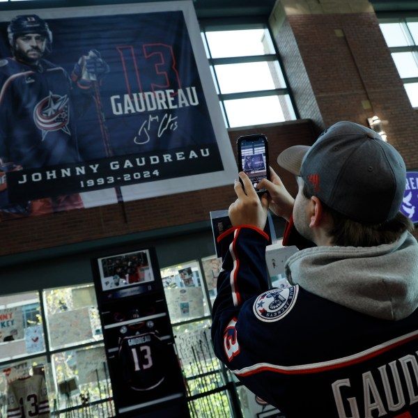 Troy Ward, of Dayton, takes photos of a memorial of Columbus Blue Jackets' Johnny Gaudreau and his brother Matthew before the start of an NHL hockey game against the Florida Panthers. Tuesday, Oct. 15, 2024, in Columbus, Ohio. (AP Photo/Jay LaPrete)