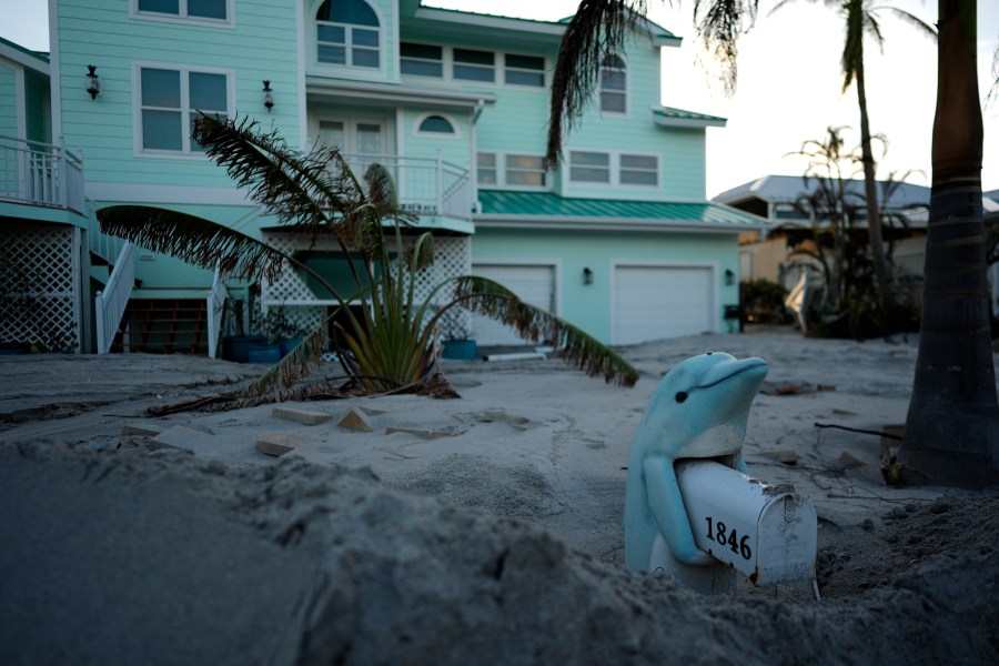 A porpoise mailbox stand is partially buried in feet of sand on Manasota Key, Fla., following Hurricane Milton, Saturday, Oct. 12, 2024. (AP Photo/Rebecca Blackwell)