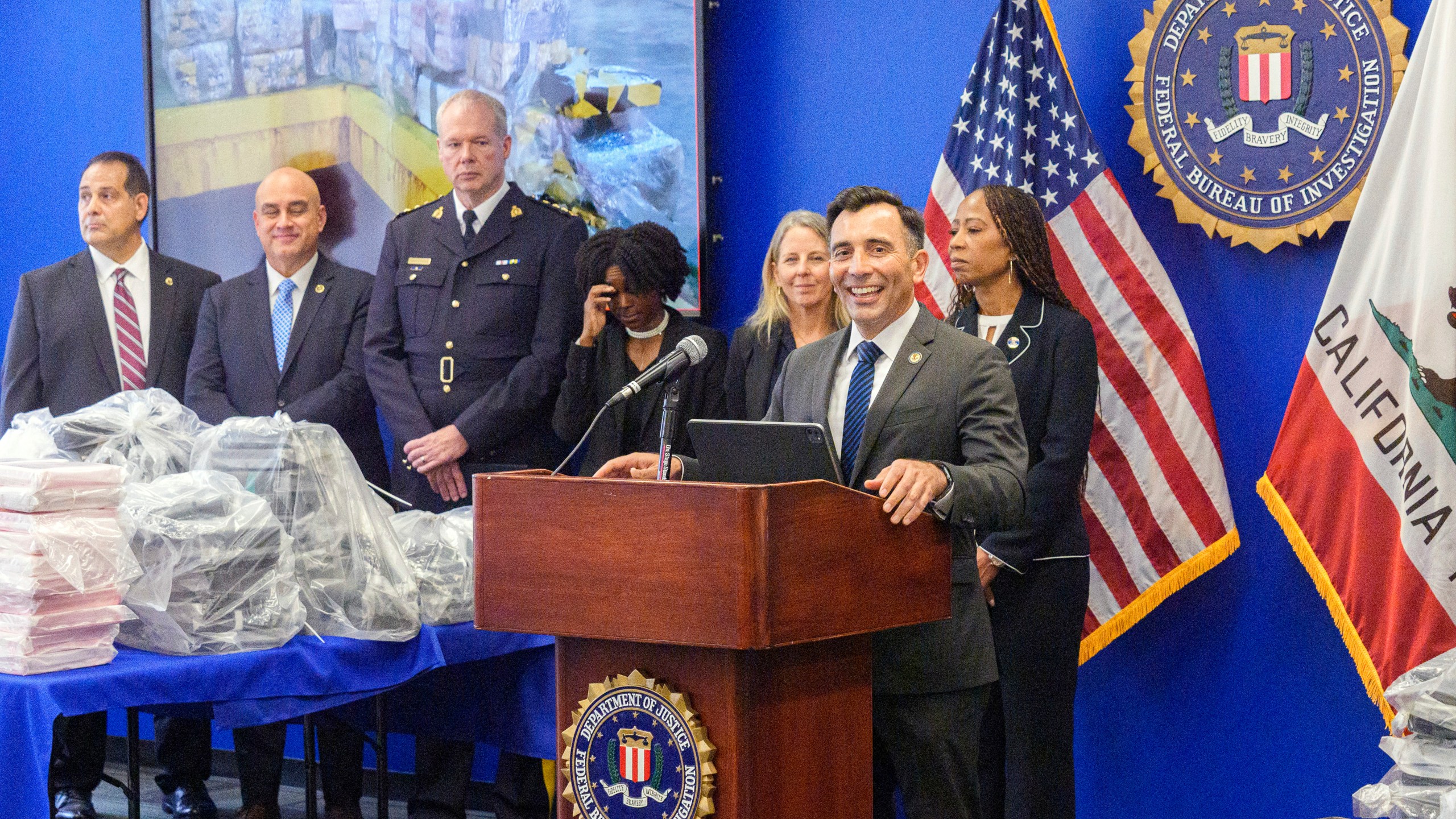 United States Attorney Martin Estrada, at podium, smiles as he's joined by federal, local, and international officials, to announce federal charges and arrests of alleged members of a transnational drug trafficking operation that routinely shipped hundreds of kilograms of cocaine from Colombia, through Mexico and Southern California, to Canada and other locations in the United States, during a news conference at the FBI offices in Los Angeles, Thursday, Oct. 17, 2024. (AP Photo/Damian Dovarganes)