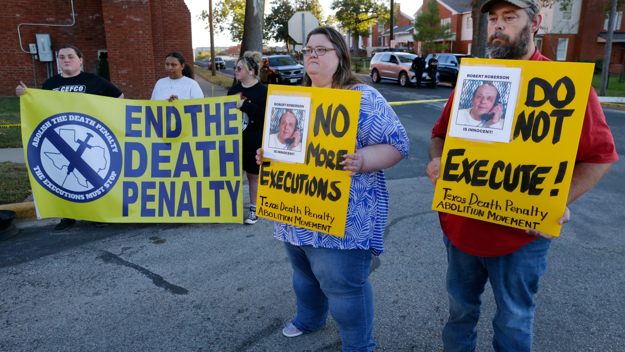 Jennifer Martin, center, and Thomas Roberson, right, older brother of condemned prisoner Robert Roberson, holds signs with others as they protest outside the prison where Roberson is scheduled for execution at the Huntsville Unit of the Texas State Penitentiary, Thursday, Oct. 17, 2024, in Huntsville, Texas. (AP Photo/Michael Wyke)