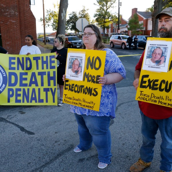 Jennifer Martin, center, and Thomas Roberson, right, older brother of condemned prisoner Robert Roberson, holds signs with others as they protest outside the prison where Roberson is scheduled for execution at the Huntsville Unit of the Texas State Penitentiary, Thursday, Oct. 17, 2024, in Huntsville, Texas. (AP Photo/Michael Wyke)