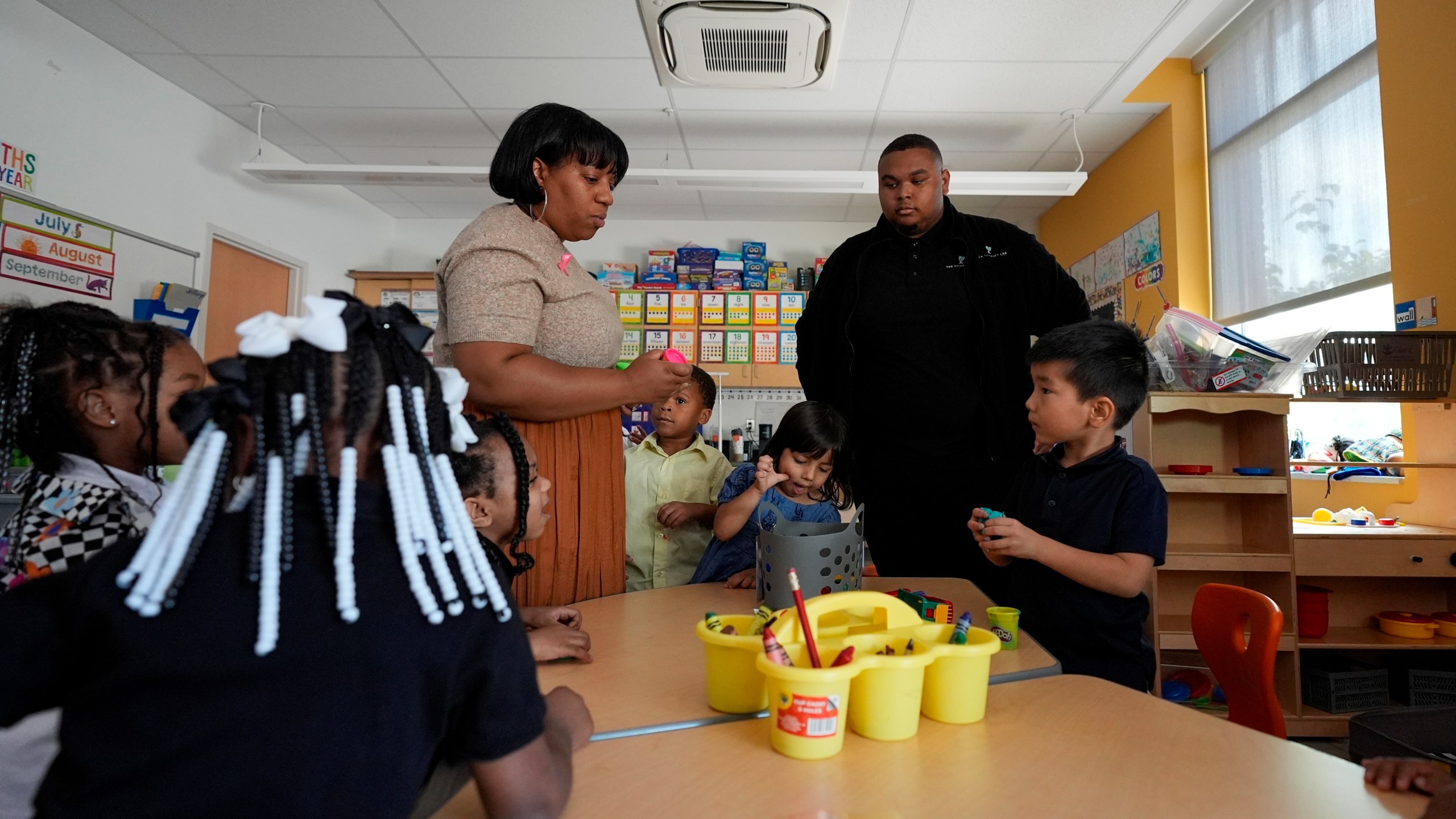 Preschool teacher Bridget Jeffreys and Leading Men fellow Davontez Johnson are surrounded by students while distributing playdough for an activity, Thursday, Oct. 3, 2024, at Dorothy I. Height Elementary School in Baltimore. (AP Photo/Stephanie Scarbrough)