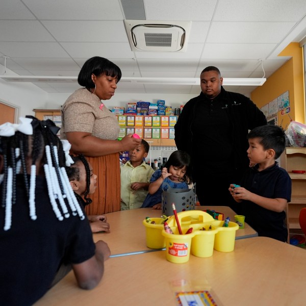 Preschool teacher Bridget Jeffreys and Leading Men fellow Davontez Johnson are surrounded by students while distributing playdough for an activity, Thursday, Oct. 3, 2024, at Dorothy I. Height Elementary School in Baltimore. (AP Photo/Stephanie Scarbrough)