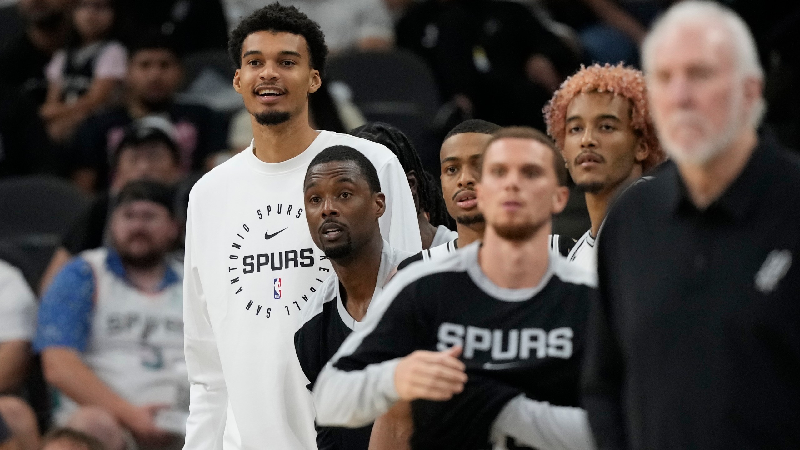 San Antonio Spurs center Victor Wembanyama, left, watches from the bench during the second half of a preseason NBA basketball game against the Oklahoma City Thunder in San Antonio, Monday, Oct. 7, 2024. (AP Photo/Eric Gay)