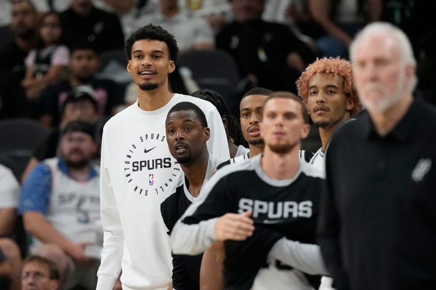 San Antonio Spurs center Victor Wembanyama, left, watches from the bench during the second half of a preseason NBA basketball game against the Oklahoma City Thunder in San Antonio, Monday, Oct. 7, 2024. (AP Photo/Eric Gay)