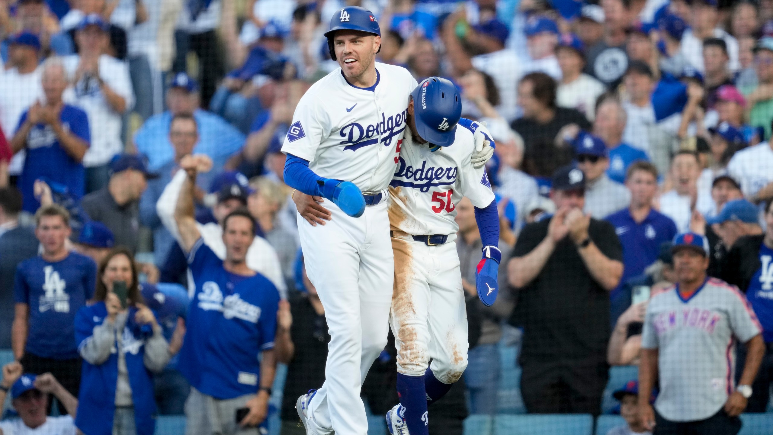 Los Angeles Dodgers' Freddie Freeman, left, and Mookie Betts celebrate after they scored on a single by Max Muncy during the first inning in Game 1 of a baseball NL Championship Series against the New York Mets, Sunday, Oct. 13, 2024, in Los Angeles. (AP Photo/Ashley Landis)