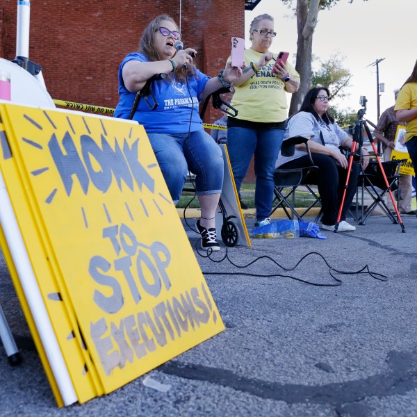 Dani Allen, center left with microphone, an anti-death penalty advocate, speaks during a protest outside the prison where Robert Roberson is scheduled for execution at the Huntsville Unit of the Texas State Penitentiary, Thursday, Oct. 17, 2024, in Huntsville, Texas. (AP Photo/Michael Wyke)