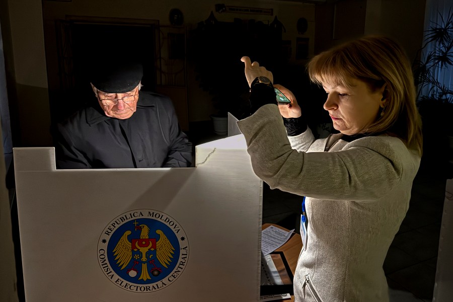 An election official assists a voter with her mobile phone flashlight during a power failure in Chisinau, Moldova, Sunday, Oct. 20, 2024, during a presidential election and a referendum on whether to enshrine in the Constitution the country's path to European Union membership. (AP Photo/Nicolae Dumitrache)