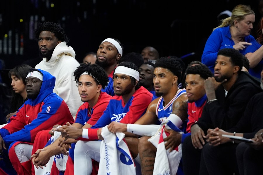 Philadelphia 76ers' Joel Embiid, top left, and Paul George, bottom right, watch from the bench during the first half of an NBA basketball game against the Milwaukee Bucks, Wednesday, Oct. 23, 2024, in Philadelphia. (AP Photo/Matt Slocum)